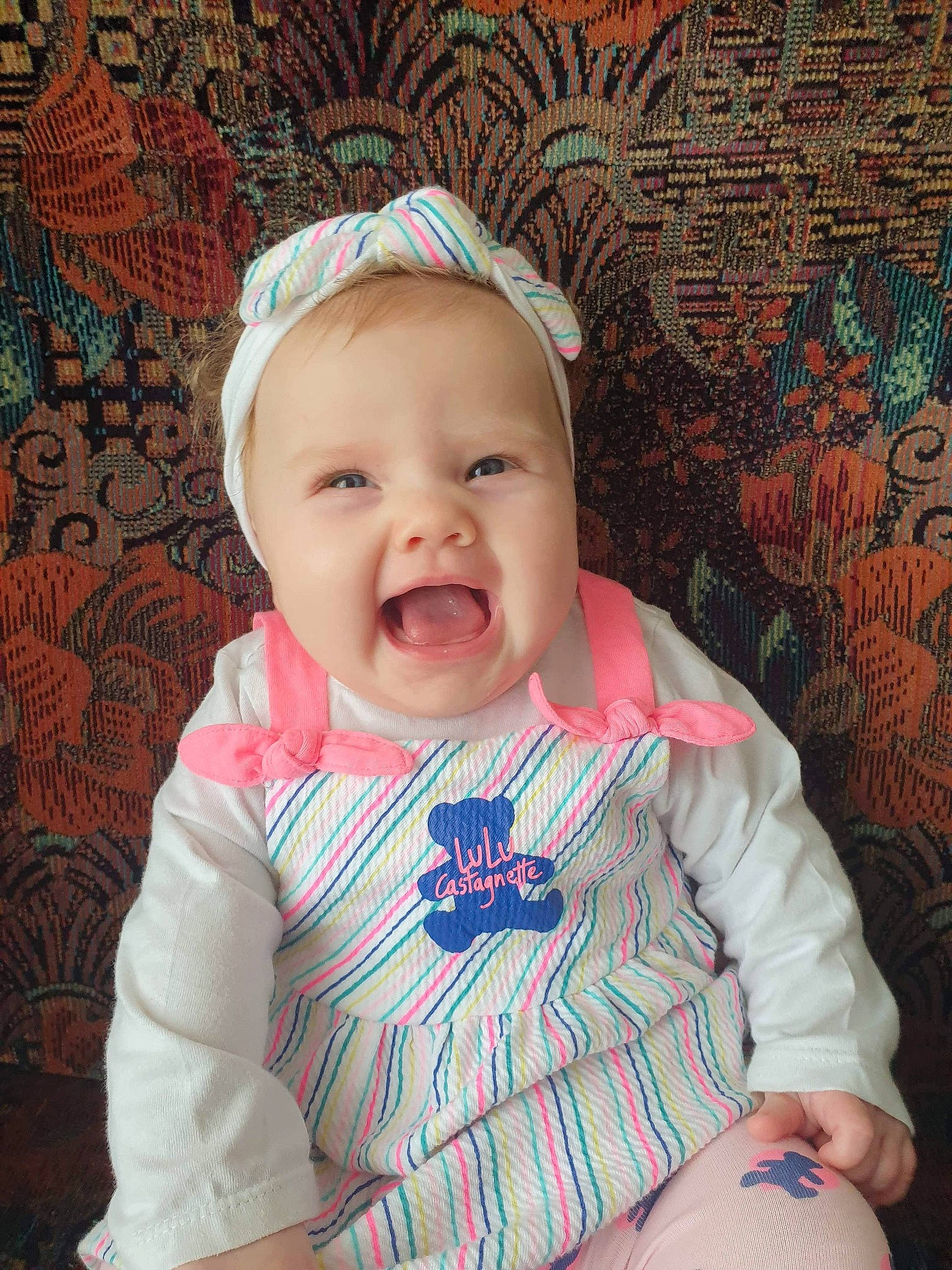 Emy a rejoint le concours — aidez-le/la à gagner de superbes lots ! baby, baby_laughing, baby_products, baby_toddler_clothing, bonnet, cheek, child, costume_accessory, creative_arts, hair_accessory, headband, headpiece, lip, pattern, peach, person, pink, skin, toddler, tongue