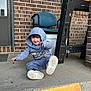 Zander is registered to the contest to win money with this photo: toddler, child, hoodie, sneakers, concrete, step, brick_wall, chair, workbench, outdoor, casual, smile, sitting, playful, young_child, daylight, curly_hair, fun, person, clothing