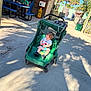 Zander is registered to the contest to win money with this photo: child, stroller, outdoor, sidewalk, toy, person, man, table, bench, tree, shadow, sunlight, fence, hat, shoes, clothing, backpack, greenery, walking, casual