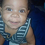 Emoni joined the competition — help win amazing prizes! baby, child, smiling, face, eyes, striped_clothing, sleeveless, skin, curly_hair, happy, infant, cute, portrait, closeup, sitting, indoors, person, young_child, blue_background, joyful