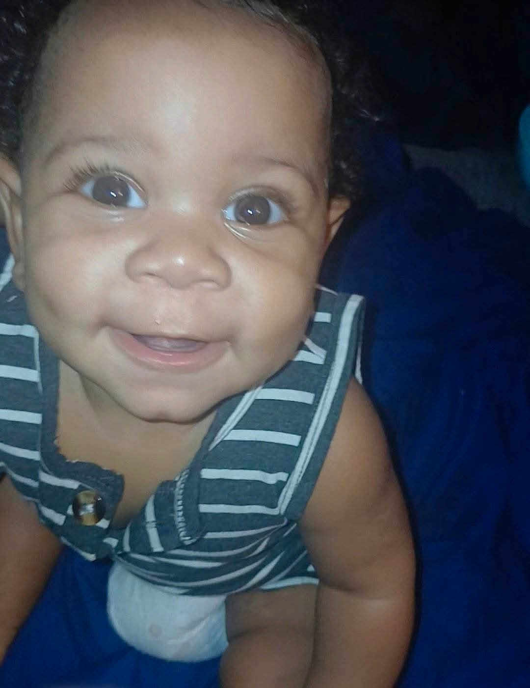 Emoni joined the competition — help win amazing prizes! baby, child, smiling, face, eyes, striped_clothing, sleeveless, skin, curly_hair, happy, infant, cute, portrait, closeup, sitting, indoors, person, young_child, blue_background, joyful