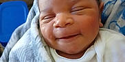 Emoni joined the competition — help win amazing prizes! baby, newborn, smiling, blanket, pillow, face, infant, closeup, sleepy, cozy, indoors, cute, child, person, soft, warm, white_clothing, resting, peaceful, portrait