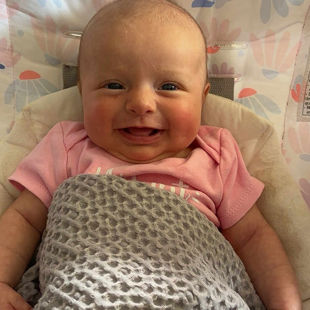 Oaklee joined the competition — help win amazing prizes! baby, baby_girl, blanket, cheeks, child, cozy, cute, face, happy, head, indoor, infant, patterned, pink_clothing, portrait, seat, skin, smiling, textured_blanket, young