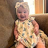 baby, child, smiling, dress, headband, bow, butterfly_pattern, couch, indoor, happy, person, infant, sitting, sunlight, warm_light, cute, portrait, fabric, furniture, skin