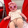 baby, child, sunglasses, headband, red_chair, beige_pants, white_shirt, bunny_print, outdoor, relaxing, cute, face, person, infant, seated, summer, fashion, accessory, smiling, leisure