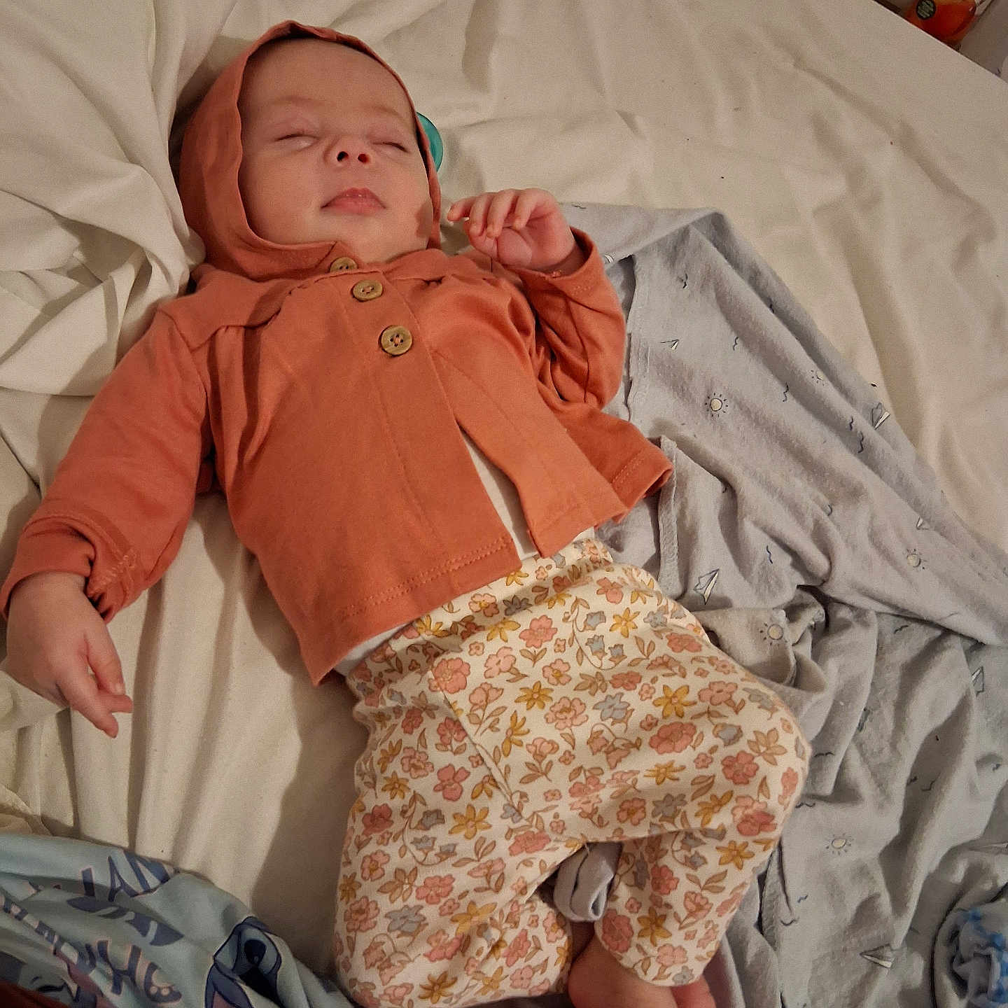 Magdalen is registered to the contest to win money with this photo: baby, sleeping, bed, blanket, clothing, floral_pattern, hoodie, infant, indoors, peaceful, person, pajamas, resting, soft_fabric, toddler, white_sheet, lying_down, cute, cozy, child