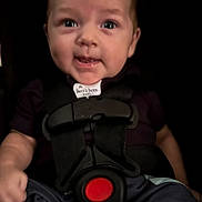 Emiliano is registered to the contest to win money with this photo: baby, infant, child, portrait, face, smiling, seated, harness, safety_harness, car_seat, red_buckle, dark_background, close_up, indoors, clothing, short_hair, blue_eyes, happy, looking_at_camera, photograph