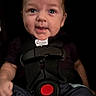 baby, infant, child, portrait, face, smiling, seated, harness, safety_harness, car_seat, red_buckle, dark_background, close_up, indoors, clothing, short_hair, blue_eyes, happy, looking_at_camera, photograph