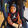 baby, child, infant, stroller, portrait, sitting, wide_eyes, indoors, black_clothing, headband, sportswear, sneakers, bib, nike, jordan, chair, floor, fashion, closeup, happy