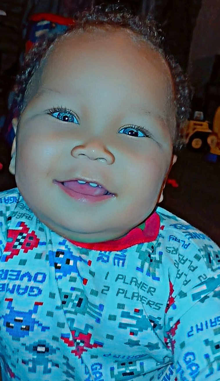 Zaedyn is registered to the contest to win money with this photo: baby, child, smiling, face, blue_eyes, curly_hair, teeth, shirt, patterned_clothing, indoor, closeup, happy, person, portrait, cute, infant, childhood, bright_eyes, colorful, young