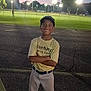 child, boy, baseball_uniform, cap, smiling, parking_lot, dusk, sports_field, lights, trees, grass, outdoor, person, young, happy, athlete, sports, standing, crossed_arms, casual