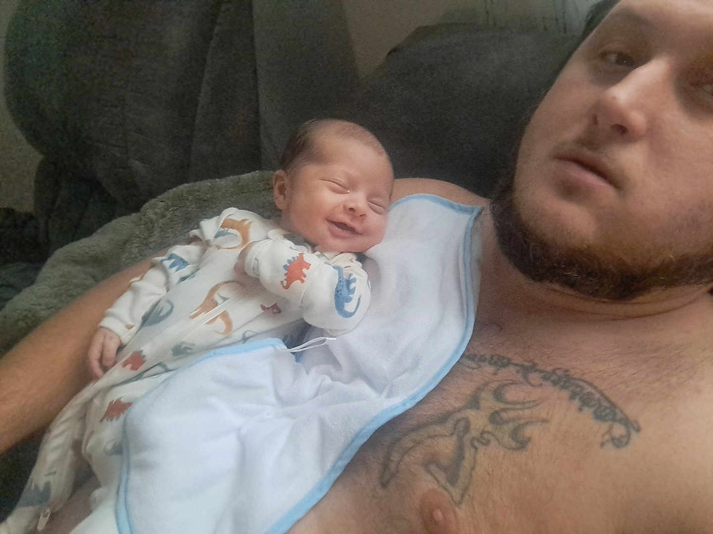 Asher joined the competition — help win amazing prizes! baby, man, tattoo, smile, pajamas, dinosaur_pattern, blanket, couch, relaxing, indoor, portrait, skin, facial_hair, child, infant, clothing, comfort, person, happy, resting