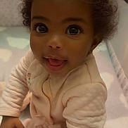 Sevyn is registered to the contest to win money with this photo: baby, infant, child, face, eyes, smile, curly_hair, onesie, pajamas, plush, blanket, crib, hand, portrait, closeup, indoor, happy, sitting, skin, toy