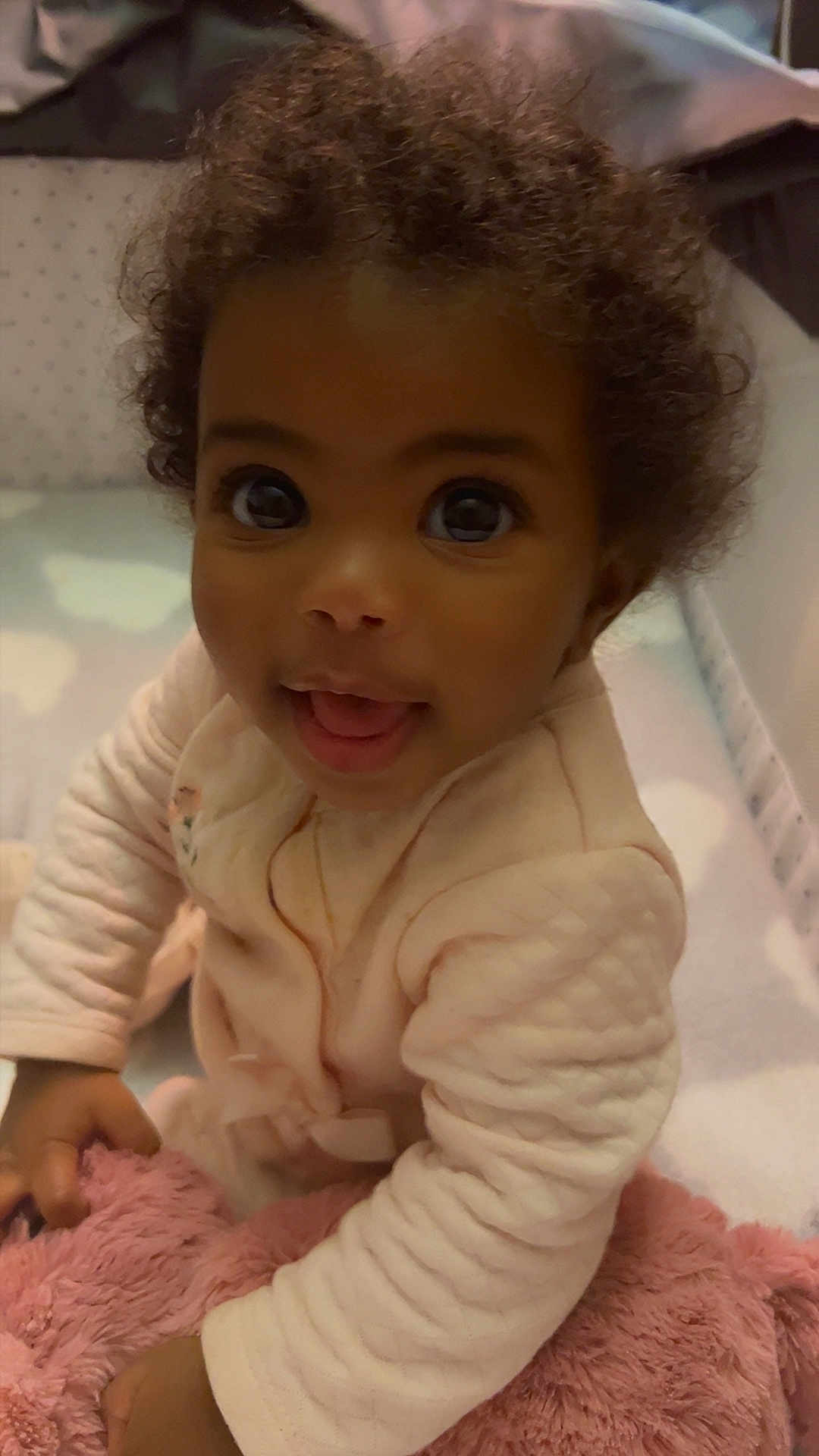 Sevyn is registered to the contest to win money with this photo: baby, infant, child, face, eyes, smile, curly_hair, onesie, pajamas, plush, blanket, crib, hand, portrait, closeup, indoor, happy, sitting, skin, toy