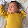 baby, blanket, child, cozy, cute, fabric, face, hand, head, indoors, infant, newborn, pale_skin, pastel_colors, peaceful, rainbow_pattern, resting, sleeping, soft_texture, yellow_onesie