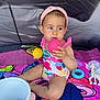 toddler, child, swimsuit, headband, toy, ball, pink_ball, yellow_ball, giraffe_toy, colorful_towel, bucket, indoor, sitting, curious, playtime, baby, person, cute, summer, play