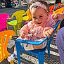 toddler, child, smiling, blue_chair, plastic_chair, headband, pink_jacket, outdoor, colorful_chairs, yellow_chair, orange_chair, pink_chair, socks, gravel_ground, daylight, person, hand, event, happy, casual_clothing