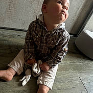 Léo participe au concours pour gagner de l'argent avec cette photo : toddler, child, indoor, plaid_shirt, light_pants, soft_toy, barefoot, floor, wooden_floor, curious_expression, pouty_face, sitting, person, young_child, cushion, wall, texture, casual_clothing, portrait, natural_light