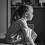 child, girl, bedroom, black_and_white, profile, braided_hair, ponytail, pajamas, patterned_pants, sitting, bed, soft_lighting, indoors, contemplative, young, portrait, furniture, blurred_background, casual_clothing, home