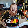 baby, child, smile, piano, toy, activity_center, indoor, colorful, face, clothing, hand, floor, carpet, furniture, playtime, infant, happy, living_room, footwear, baby_bib