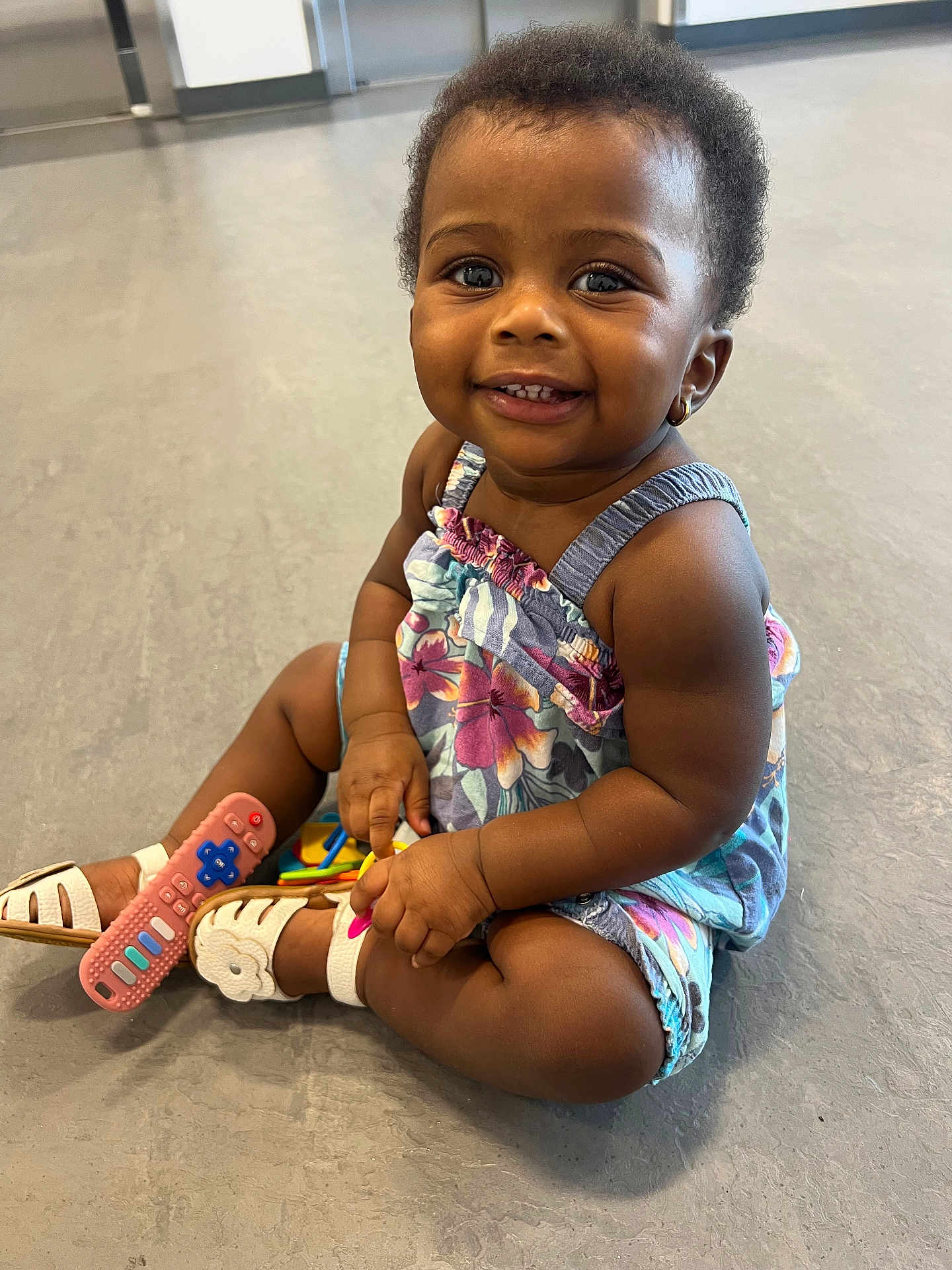 Melody joined the competition — help win amazing prizes! toddler, child, smiling, sitting, floor, toy, remote_control, sandals, floral_dress, earring, happy, cute, indoor, person, baby, skin, arm, leg, face, eyes