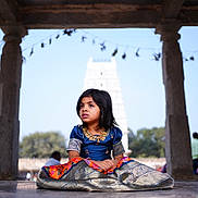 Tanvireddy is registered to the contest to win money with this photo: child, girl, traditional_clothing, sitting, floor, pavilion, stone_pillars, temple, outdoor, daylight, portrait, expression, architecture, background, nature, people, cultural, dress, young, serene