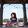 child, girl, traditional_clothing, sitting, floor, pavilion, stone_pillars, temple, outdoor, daylight, portrait, expression, architecture, background, nature, people, cultural, dress, young, serene