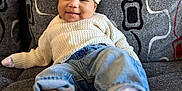 Stori is registered to the contest to win money with this photo: baby, infant, smiling, hat, knit_hat, sweater, jeans, white_shoes, couch, patterned_cushion, gray_couch, indoor, child, cute, comfortable, relaxed, portrait, cozy, happy, small_ears_hat