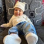 baby, infant, smiling, hat, knit_hat, sweater, jeans, white_shoes, couch, patterned_cushion, gray_couch, indoor, child, cute, comfortable, relaxed, portrait, cozy, happy, small_ears_hat