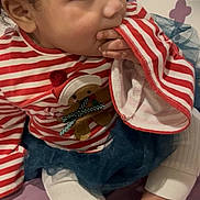 Stori joined the competition — help win amazing prizes! toddler, child, striped_shirt, red, white, gingerbread_man, hand_in_mouth, sitting, blue_tutu, bedspread, purple, curly_hair, cute, indoors, clothing, foot, skin, face, young_child, playful