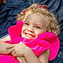 child, girl, smiling, curly_hair, blonde, pink_dress, outdoor, blanket, happy, face, portrait, cute, joyful, childhood, fashion, person, lying_down, playful, sunlight, accessory