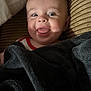baby, blanket, smiling, tongue_out, cushion, striped, infant, face, happy, child, soft_light, indoors, portrait, cute, wrapped, cozy, skin, head, expression, young