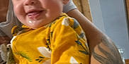 Stormy joined the competition — help win amazing prizes! baby, child, smile, yellow_clothing, floral_pattern, drool, tattoo, bracelets, arm, indoor, person, happy, face, infant, cute, holding, closeup, portrait, skin, head