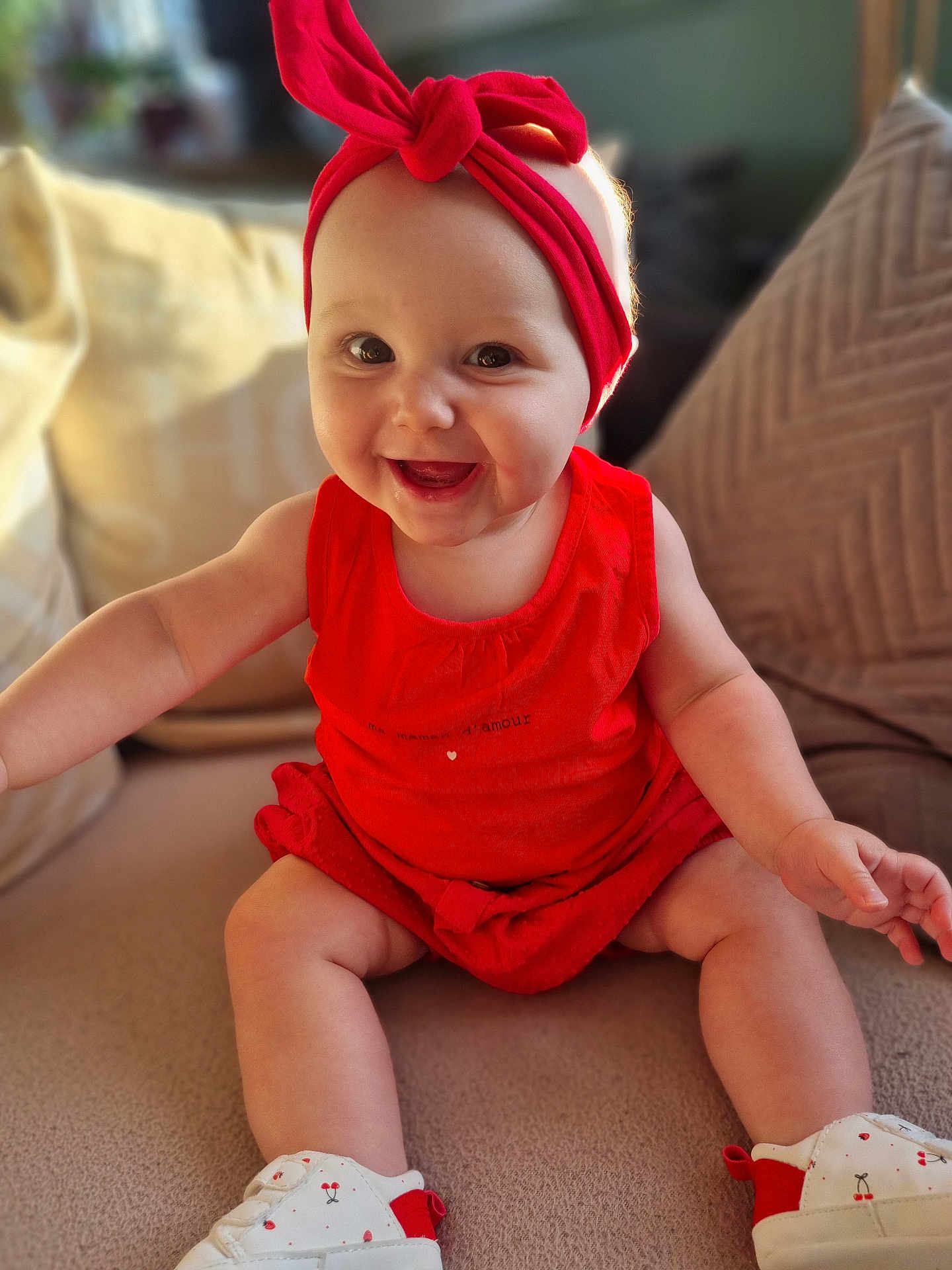 Lyana participe au concours pour gagner de l'argent avec cette photo : baby, child, smiling, red_clothing, headband, sitting, couch, cushion, happy, indoors, footwear, shoes, cute, person, portrait, infant, skin, furniture, closeup, young