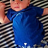 baby, infant, blue_shirt, checkered_shorts, striped_background, lying_down, face, eyes, skin, clothing, child, cute, portrait, happy_text, user_overlay, newborn, expression, arms, legs, casual