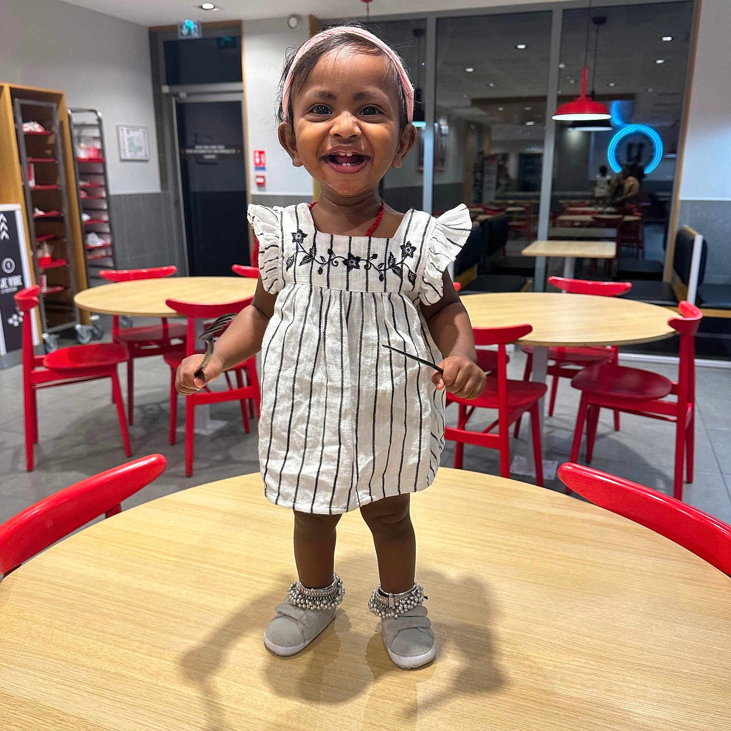 Kaniesha participe au concours pour gagner de l'argent avec cette photo : anklets, background, cafe, ceiling, child, dress, floor, furniture, happy, headband, indoor, light, person, red_chair, reflection, smile, table, toddler, window, wooden_table