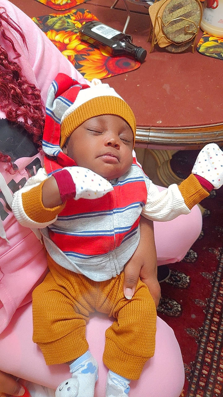 Wisdom is registered to the contest to win money with this photo: baby, baby_toddler_clothing, carmine, child, christmas_eve, event, fictional_character, flooring, fun, happy, headwear, holiday, lap, person, play, red, sitting, sleeve, thigh, thumb