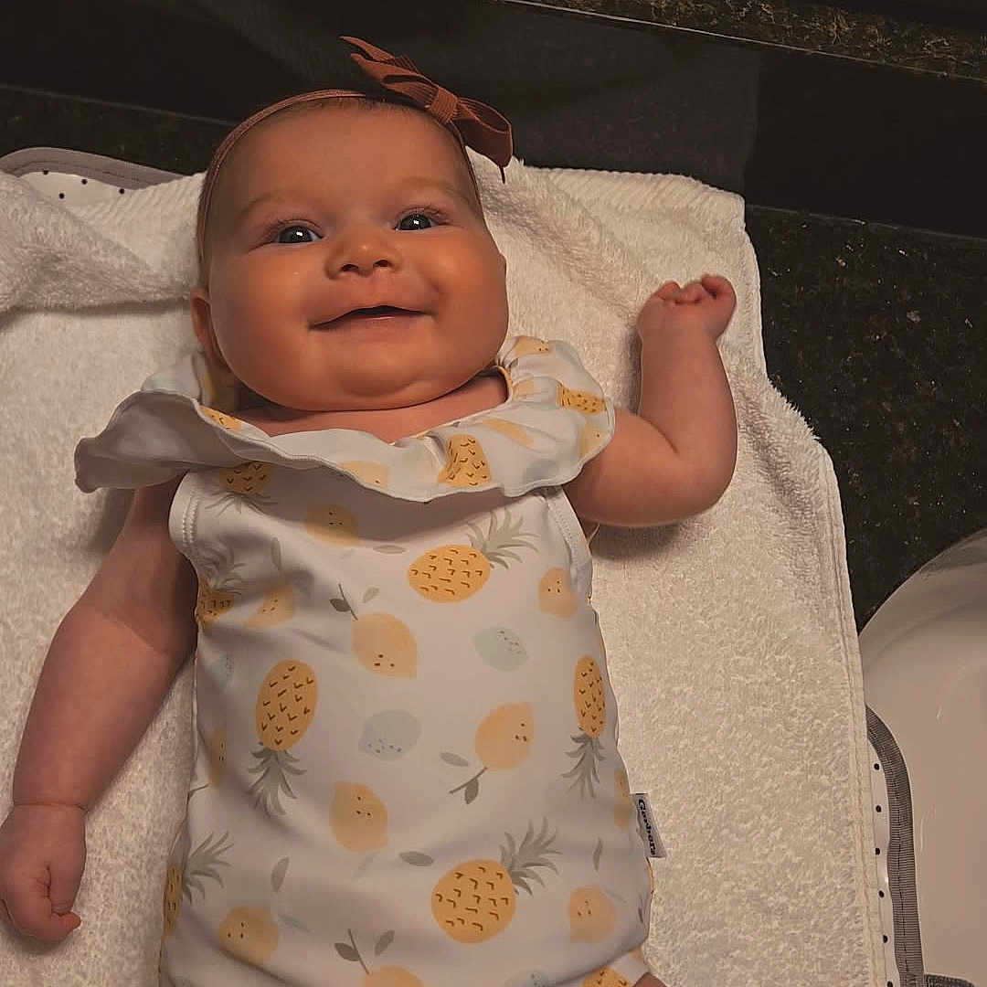 Marceline is registered to the contest to win money with this photo: arm, baby, bow, child, cute, hand, happy, headband, indoors, infant, lying_down, mirror, onesie, pineapple_pattern, portrait, reflection, skin, smiling, towel, white