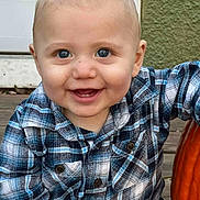 River is registered to the contest to win money with this photo: baby, child, smile, blue_eyes, plaid_shirt, pumpkin, autumn, outdoor, porch, wooden_floor, cute, happy, face, person, seasonal, fall, sitting, infant, casual_clothing, closeup