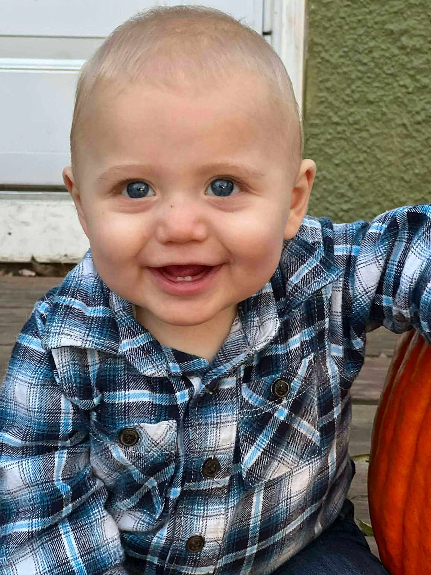 River is registered to the contest to win money with this photo: baby, child, smile, blue_eyes, plaid_shirt, pumpkin, autumn, outdoor, porch, wooden_floor, cute, happy, face, person, seasonal, fall, sitting, infant, casual_clothing, closeup