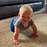Holden is registered to the contest to win money with this photo: baby, crawling, carpet, indoor, smiling, child, blonde_hair, leather_couch, playpen, home, floor, cute, person, young_child, happy, toddler, casual_clothing, gray_shirt, blue_pants, living_room