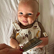 Niall is registered to the contest to win money with this photo: baby, child, smile, drool, sunglasses, overalls, animal_print, hand, person, cute, infant, clothing, bed, fabric, happy, portrait, skin, eyewear, face, toddler