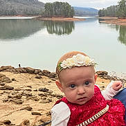 Ellie-Mae is registered to the contest to win money with this photo: baby, child, dress, headband, flower, lake, water, rocks, outdoor, nature, trees, hill, sky, cloudy, portrait, person, red_dress, scenic, reflection, calm