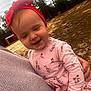 baby, toddler, child, face, red_headband, bow, pink_dress, floral_pattern, smile, portrait, close_up, person_holding_child, hand, sweater, outdoor, trees, dirt_ground, barn, overcast_sky, grass