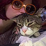 person, cat, tabby_cat, glasses_filter, indoor, close_up, cuddle, pet, sleepy, hand, face, fur, whiskers, bed, blanket, comfort, relaxation, cute, animal, friendly