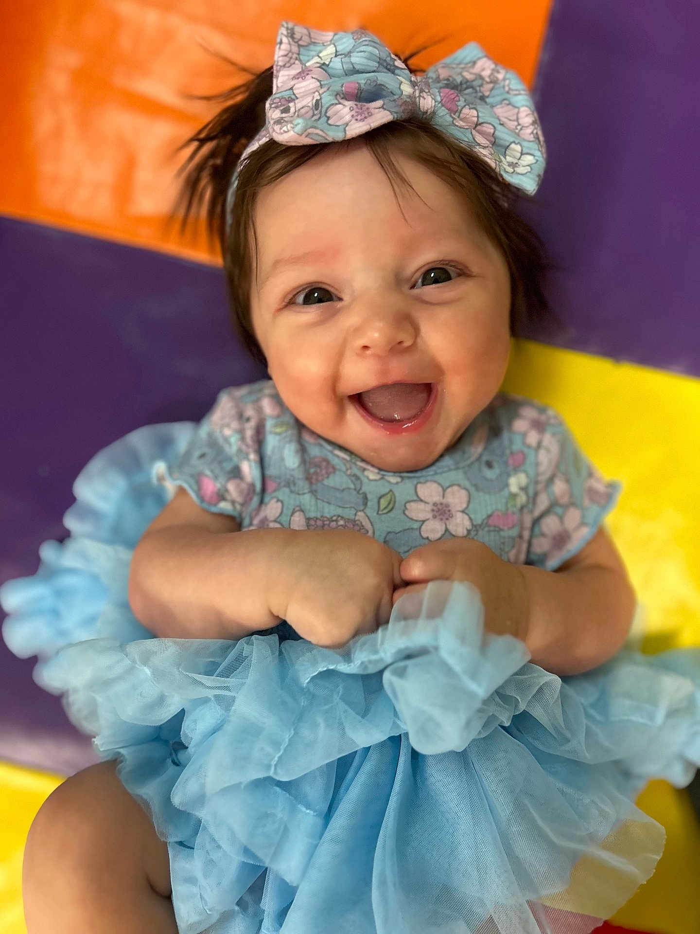 Emry is registered to the contest to win money with this photo: baby, child, smiling, dress, bow, blue, floral, happy, person, infant, cute, face, hands, sitting, colorful_background, mat, joy, young, portrait, tulle