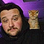 Cheese is registered to the contest to win money with this photo: man, kitten, pet, shoulder, hoodie, indoor, purple_light, casual, beard, face, young_adult, cute, animal, companion, portrait, relaxed, feline, friendship, low_light, closeup