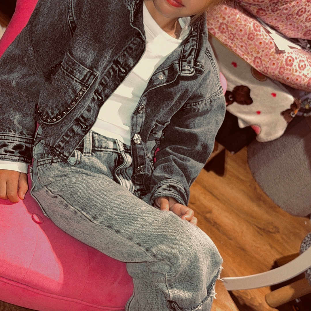 Willow participe au concours pour gagner de l'argent avec cette photo : blanket, casual_clothing, child, cozy, crossed_legs, curious_expression, denim_jacket, face, fashion, floral_pattern, furniture, hair, indoor, jeans, person, pink_chair, seated, sneakers, wooden_floor, young