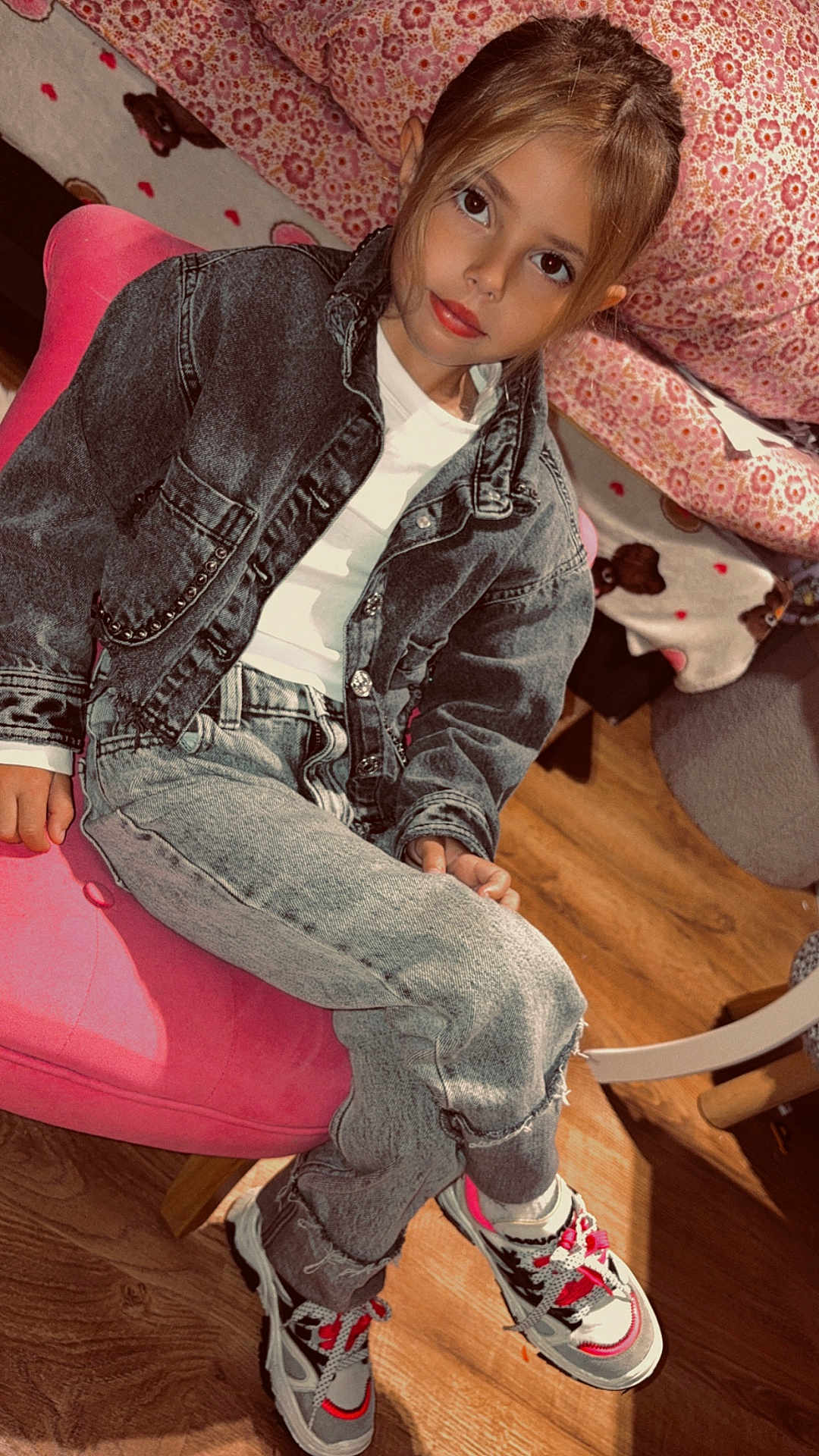 Willow participe au concours pour gagner de l'argent avec cette photo : child, denim_jacket, jeans, sneakers, pink_chair, indoor, wooden_floor, blanket, floral_pattern, face, person, seated, crossed_legs, casual_clothing, young, curious_expression, hair, fashion, cozy, furniture