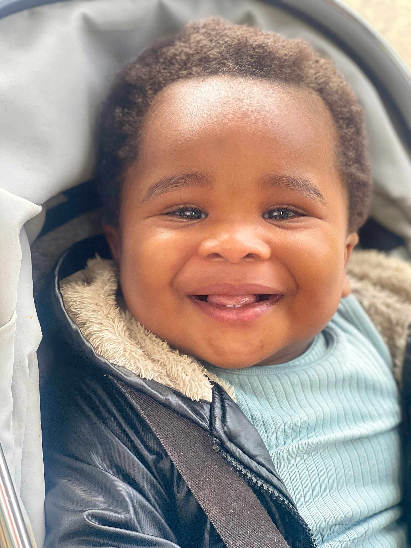 Uzochukwu joined the competition — help win amazing prizes! toddler, smiling, child, face, jacket, coat, stroller, baby, happy, cute, portrait, closeup, young_child, clothing, warm, seatbelt, outdoor, person, head, expression